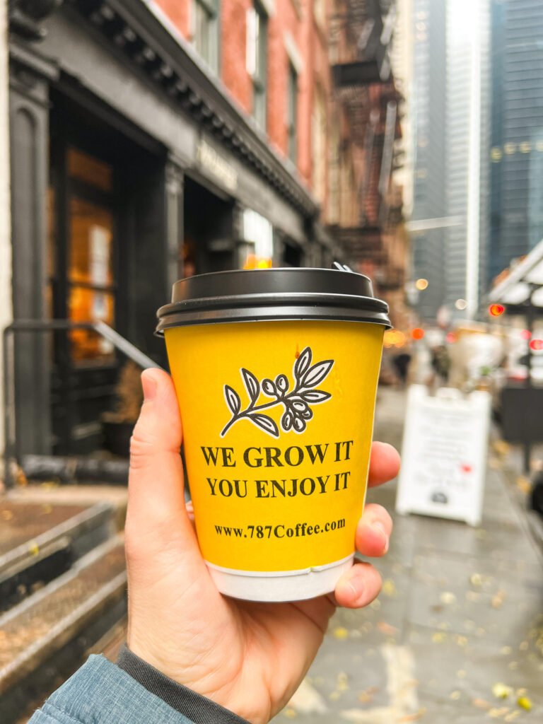Yellow paper coffee cup with black plastic lid from 787 Coffee in front of their coffee shop on Pearl Street