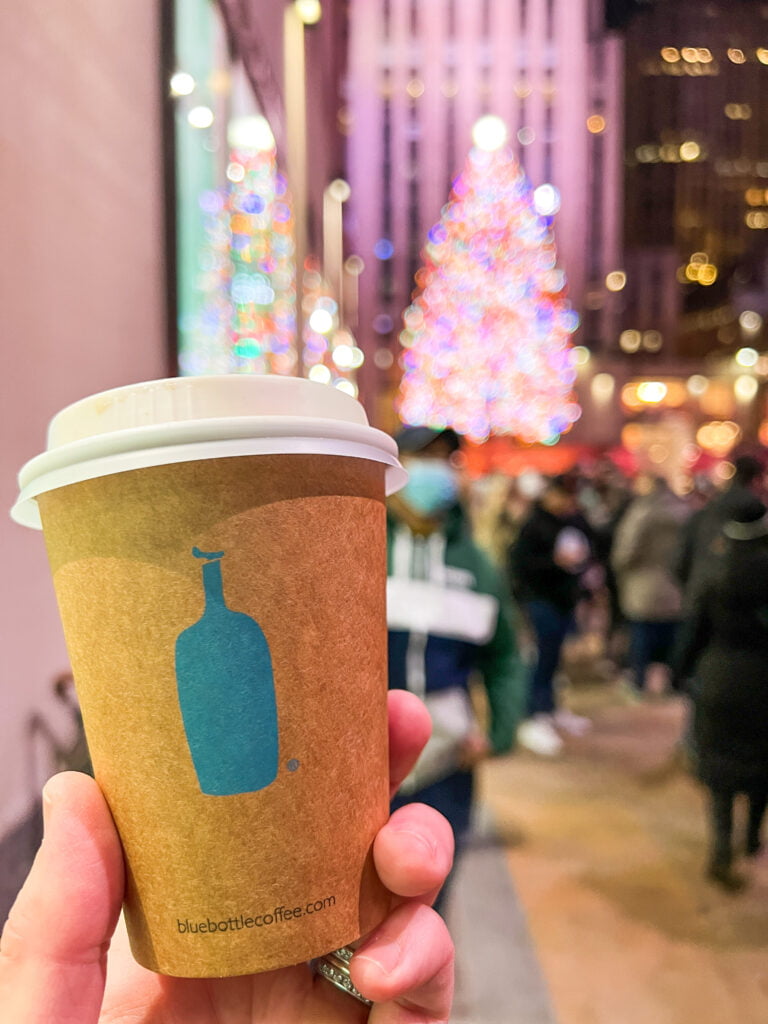 Blue Bottle Coffee cup, with the Rockefeller Center Christmas tree in the background in New York in December