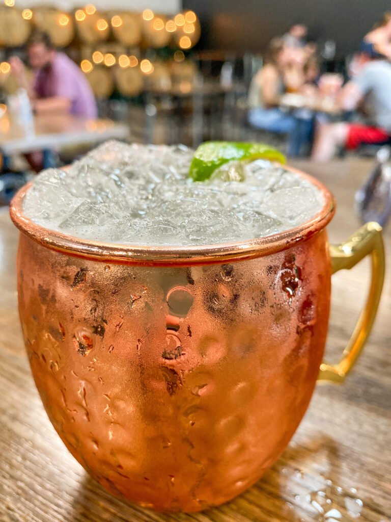 An iced Moscow Mule in a copper mug, garnished with a lime slice, sitting on a table at Rollertown Beerworks in Celina, Texas.