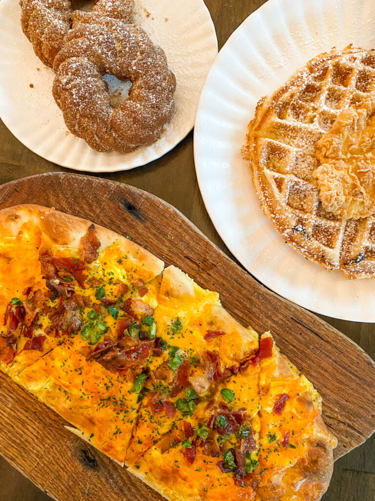 Overhead shot of three breakfast items from The Nook CKMC in Celina, TX including: Cronuts, Chicken and Waffle, and the Breakfast Flatbread.