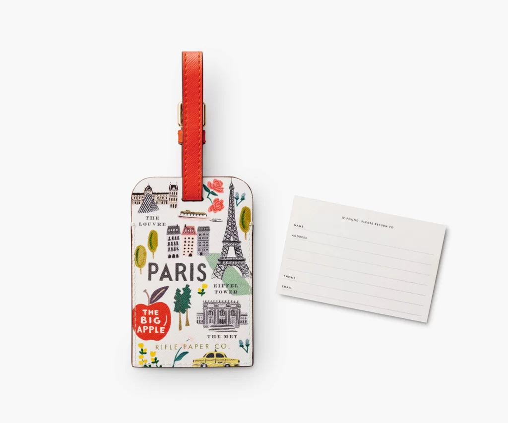 Bon Voyage luggage tag from Rifle Paper Co. with illustrations of iconic things from several major cities like Paris and NYC, and a red buckle strap
