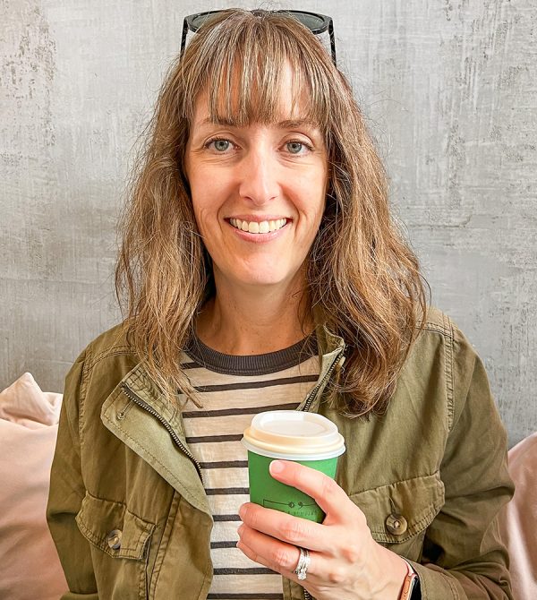Female travel blogger sitting inside a local coffee shop holding a latte in a takeaway cup